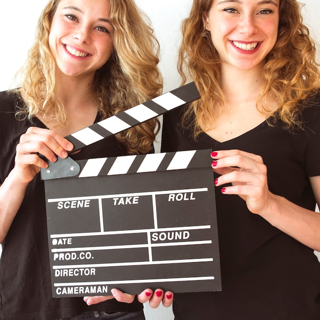 Free photo close-up of smiling wins sister holding clapperboard in hands