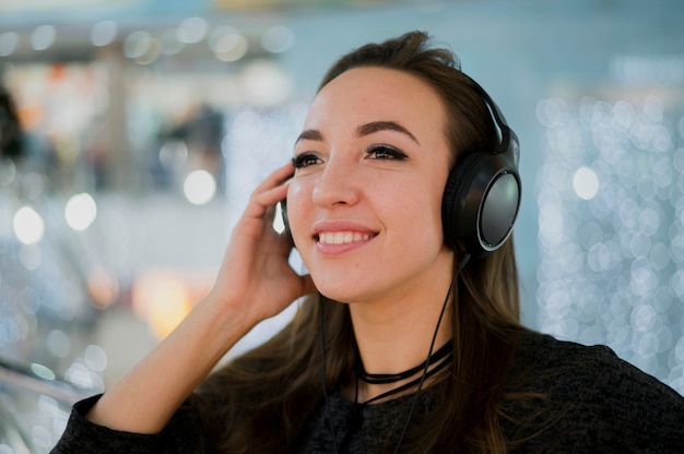 Free photo close-up smiling woman holding headphones on head in shopping mall