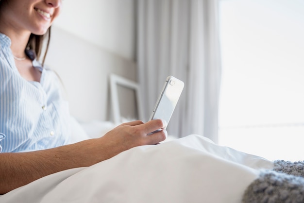 Крупным планом улыбается женщина, сидя на кровати, с помощью цифрового планшета