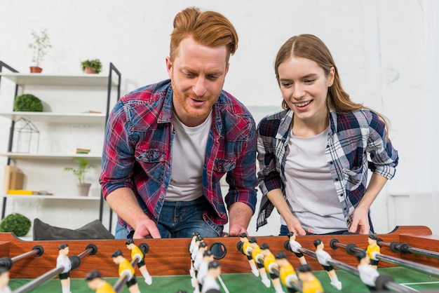 Close-up of smiling young couple playing the table soccer game at home