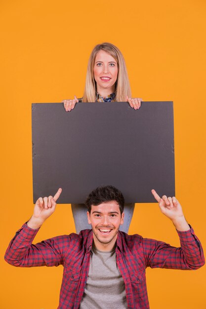 Close-up of a smiling young couple showing blank placard against an orange background