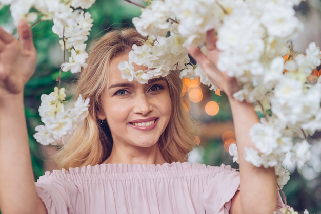 Foto gratuita primo piano della giovane donna sorridente che osserva attraverso i fiori bianchi