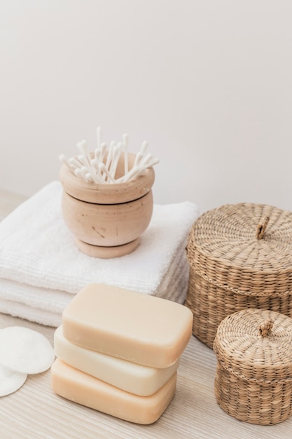 Close-up of soaps; sponge; cotton swab; towel and wicker basket on wooden surface