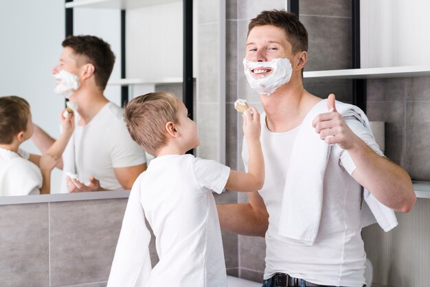 Крупным планом сына, помогая отцу для бритья бороды, показывая большой палец вверх знак