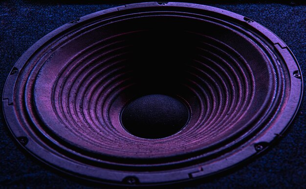 Close-up of speaker membrane on black background with colored lighting.