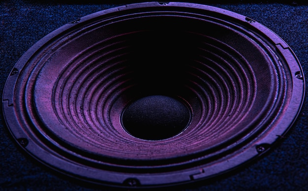 Close-up of speaker membrane on black background with colored lighting.