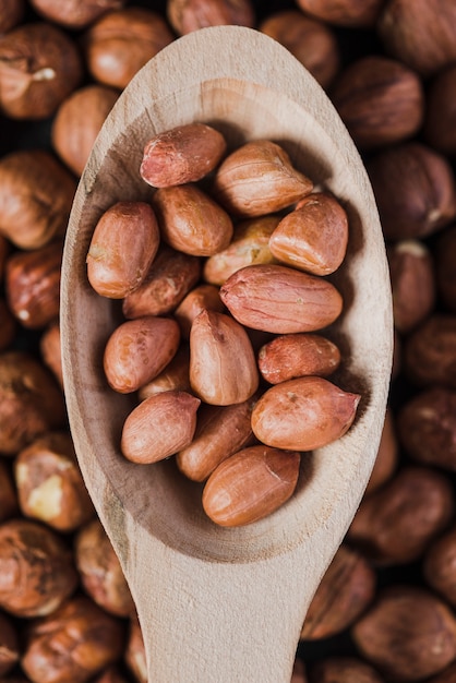 Close-up spoon with peanuts over hazelnuts