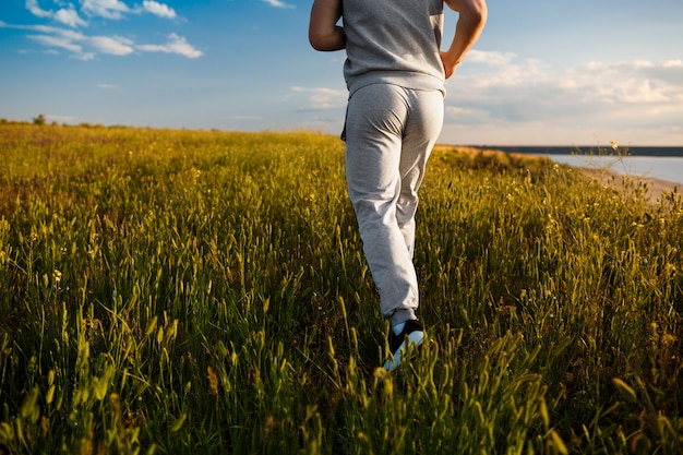 Close up of sportive man jogging in field at sunrise.