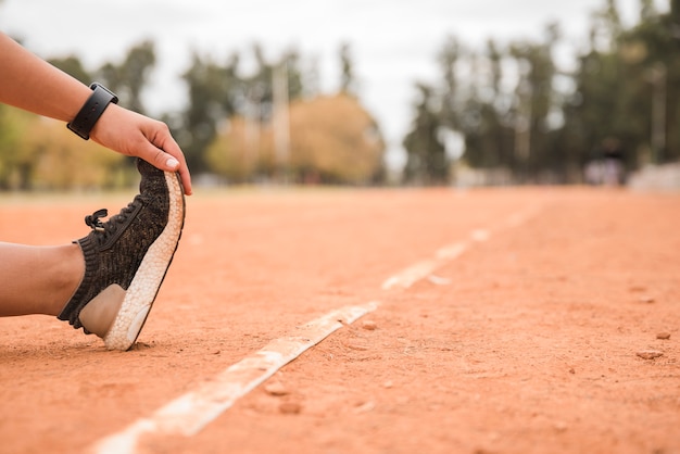 Chiuda in su della donna sportiva che si estende sulla pista dello stadio