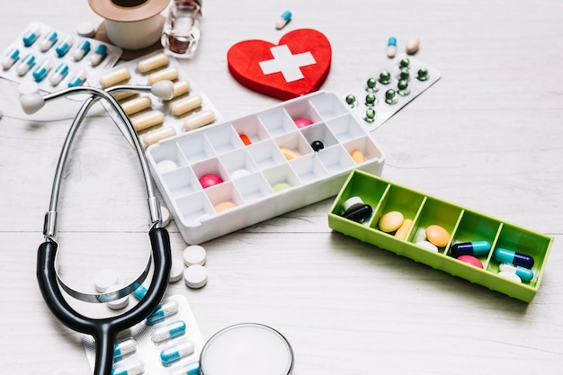 Close-up stethoscope near pills and heart with cross