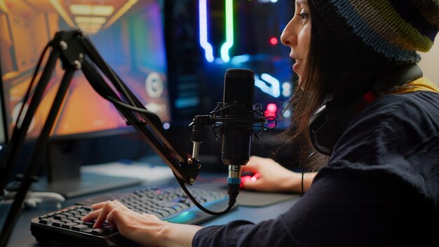 Close-up of streamer playing first person shooter video game using RGB keyboard and mouse. Gamer talking on streaming chat with other players during esport tournament late at night in gaming studio