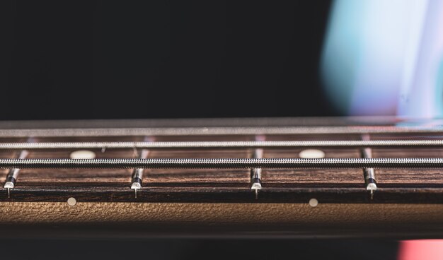 Close-up of strings on the fretboard of a bass guitar on a blurred dark background.