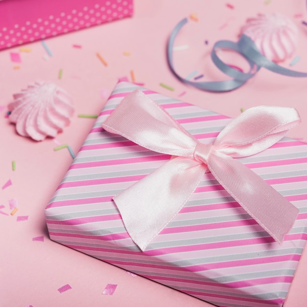 Крупный план полосатый подарочной коробке с атласным бантом против розовый фон