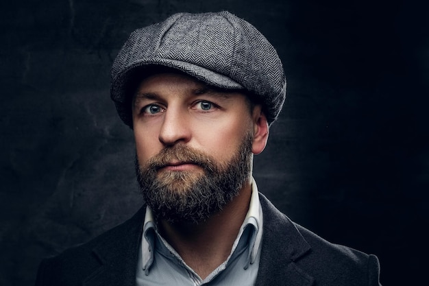 Close up studio portrait of bearded middle age male dressed in woolen suit and a tweed cap.
