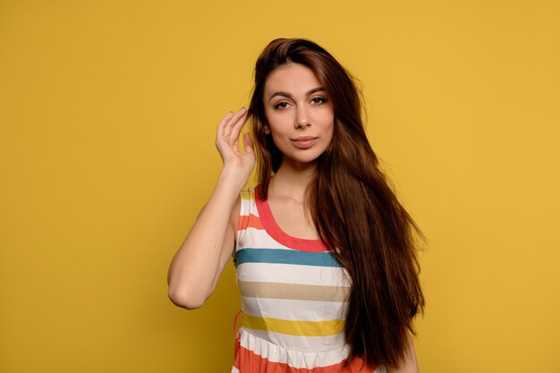 Close up studio portrait of beautiful caucasian woman with long dark hair wearing stripped dress posing