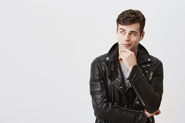 Close up studio portrait of handsome young caucasian man having concentrated thoughtful expression, frowning, keeping finger on his chin as if trying to remember something or saying: And what if.