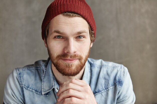 Close up studio portrait of stylish brutal young bearded European man wearing hat and jeans jacket