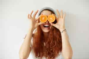 Free photo close up studio portrait of young smiling female holding halves of oranges at her eyes