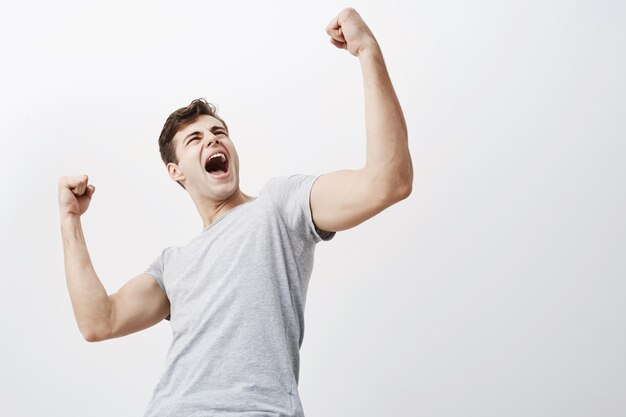 Close up of successful young caucasian male sportsman screaming Yes and raising clenched fists in the air, feeling excited. People, success, triumph, victory, winning and celebration.