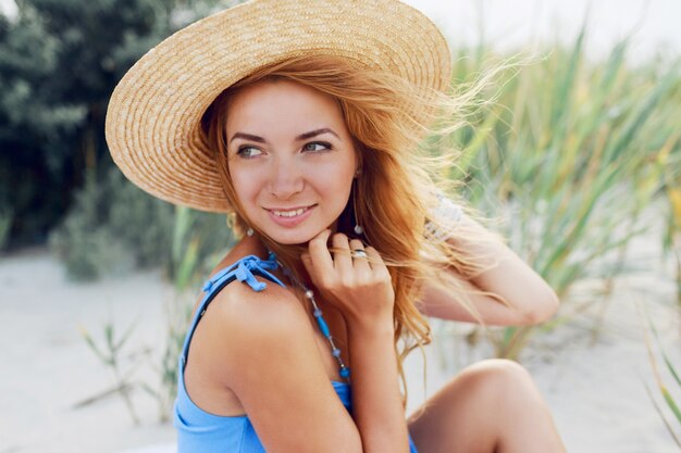 Close up summer portrait of cheerful beautiful woman in straw hat  relaxing on sunny beach on vacations. Tropical mood.