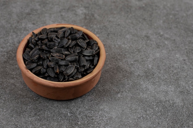 Close up of sunflower seeds in pottery bowl over grey surface