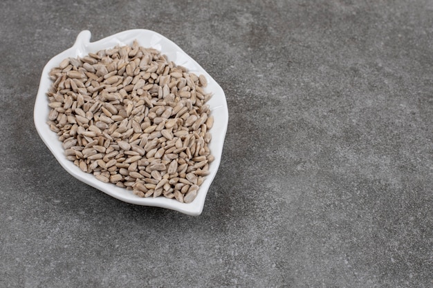 Close up of sunflower seeds on white ceramic plate over grey surface