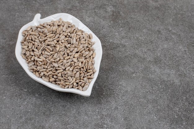 Close up of sunflower seeds on white ceramic plate over grey surface