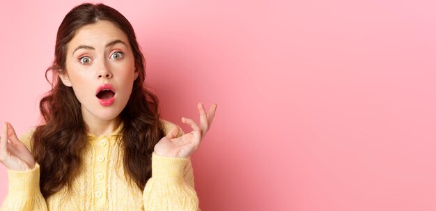 驚きと混乱の若い女性のクローズ アップは、口を開けて手を上げて、困惑した ca でカメラを凝視します。