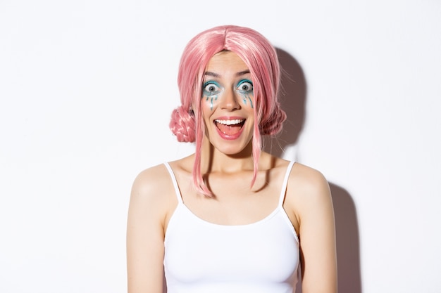 Close-up of surprised happy girl in pink wig, smiling and looking excited at camera, standing, celebrating halloween.