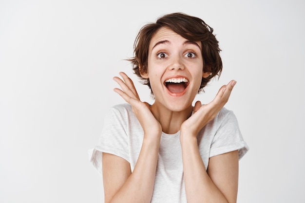 Close-up of surprised and happy woman gasping amazed, saying wow astounded, look fascinated , white wall