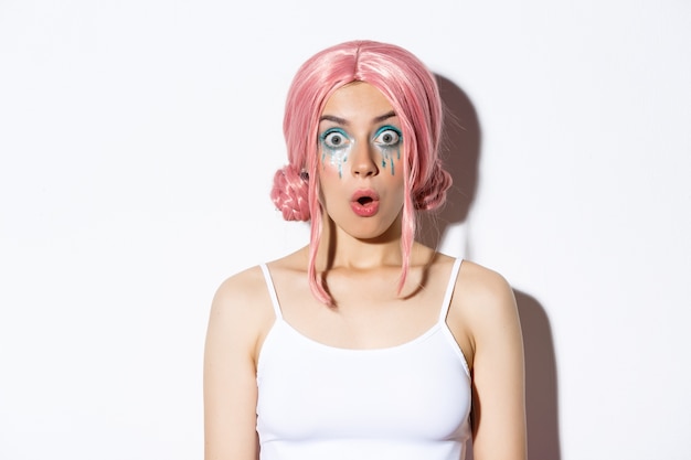 Close-up of surprised pretty girl in pink wig, gasping and looking amazed, standing.