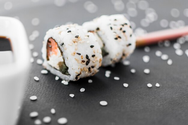 Close-up of sushi roll with sesame seeds and uncooked rice on black textured background
