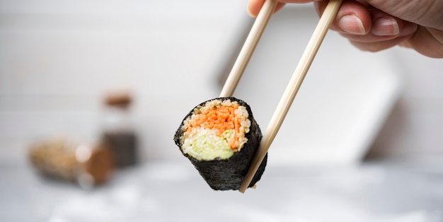 Close-up sushi roll with veggies held in chopsticks