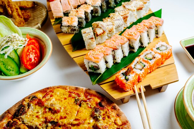 Close up of sushi set next to pizza and salad