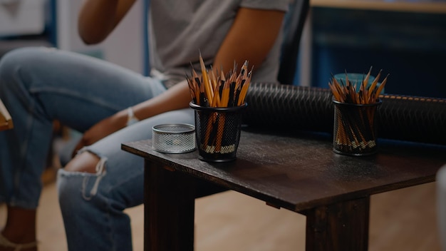 Primo piano del tavolo con strumenti artistici e matite colorate per un concetto di disegno professionale nello spazio dello studio d'arte. artista creativo afroamericano che lavora su tela capolavoro per progetto