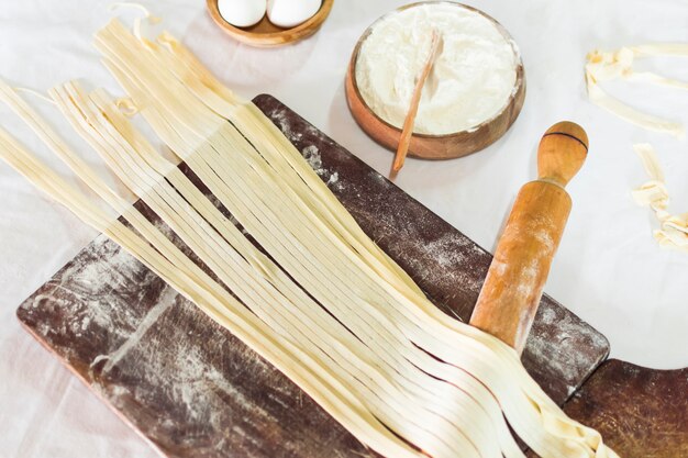 Close-up of tagliatelle pasta on wooden board with flour and rolling pins