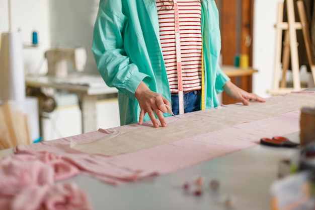 Close up tailor in colorful shirt and striped T-shirt drawing with soap on pink textile in modern sewing workshop
