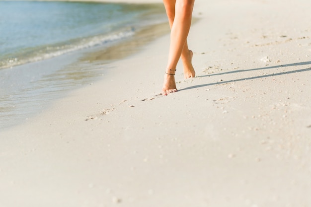 Foto gratuita primo piano dei piedi della ragazza sottile abbronzata nella sabbia. cammina vicino all'acqua. la sabbia è oro