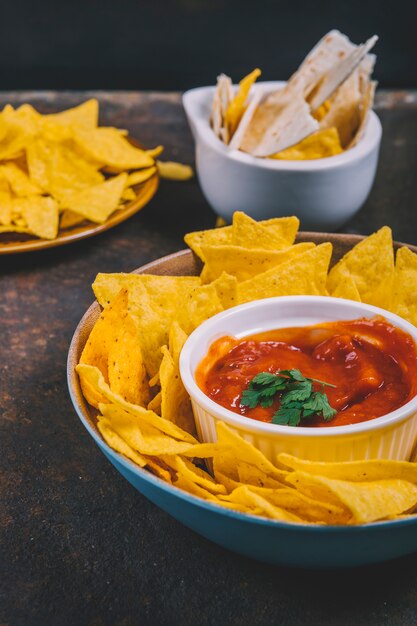 Close-up of tasty mexican nachos with salsa sauce in bowl on rusty background