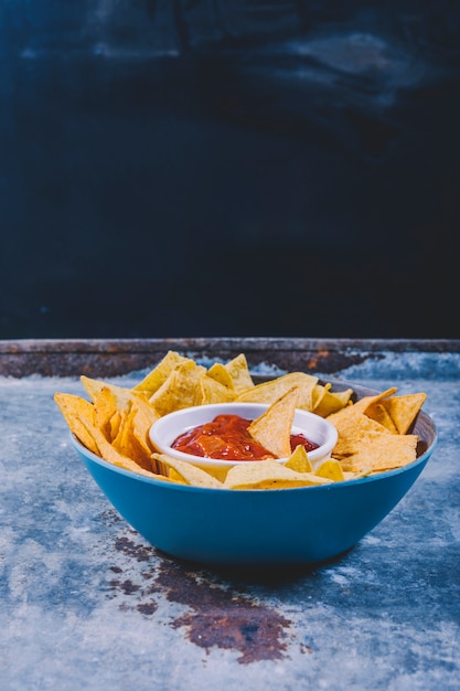 Close-up of tasty nachos and bowl with salsa sauce on metal table