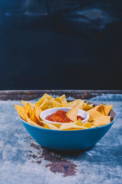 Close-up of tasty nachos and bowl with salsa sauce on metal table