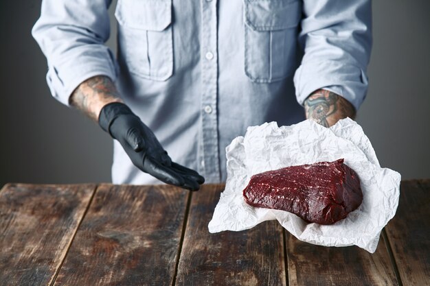 클로즈업, 검은 장갑에 문신을 한 손은 스테이크 고기를 제공합니다.