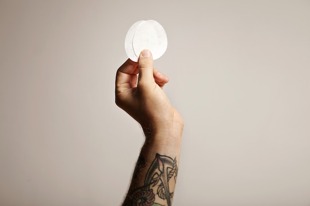 Close up of a tattooed man's hand holding two paper filters for aeropress nontraditional coffee brewer