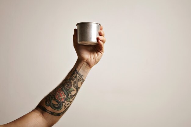 白い代替コーヒー醸造コマーシャルに鋼のトラベルカップで入れ墨の男の手のクローズアップ