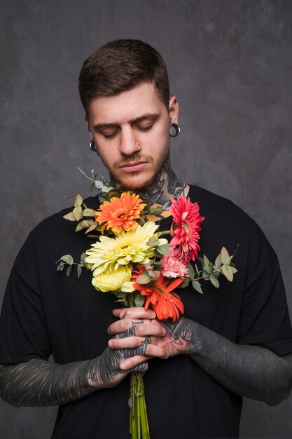 Крупный план татуированного молодого человека с цветами в руках молиться