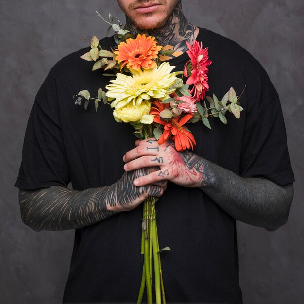 문신 된 젊은 남자의 손을 회색 벽에 꽃 꽃다발을 손에 들고 근접