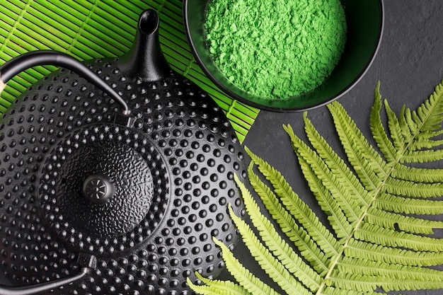 Close-up of teapot with green match tea powder and fern leaves