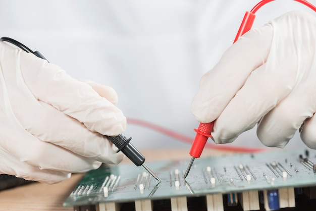 Close-up of a technician hand examining computer circuit board with digital multimeter