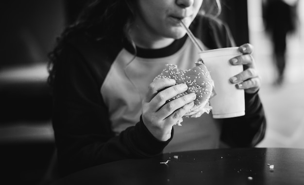 Крупный план девочка-подросток едят гамбургер концепции ожирения