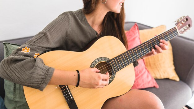 Close-up of a teenage girl sitting on sofa playing guitar at home